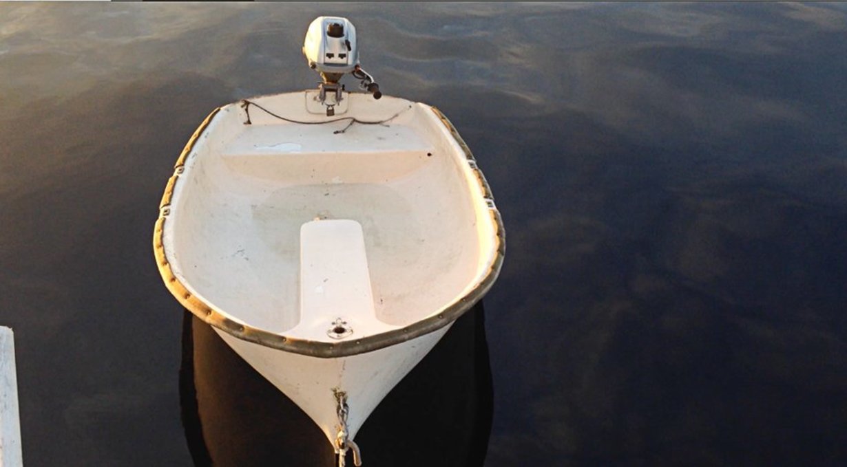 a photo of a fibreglass dinghy in the water with an outboard motor on its stern