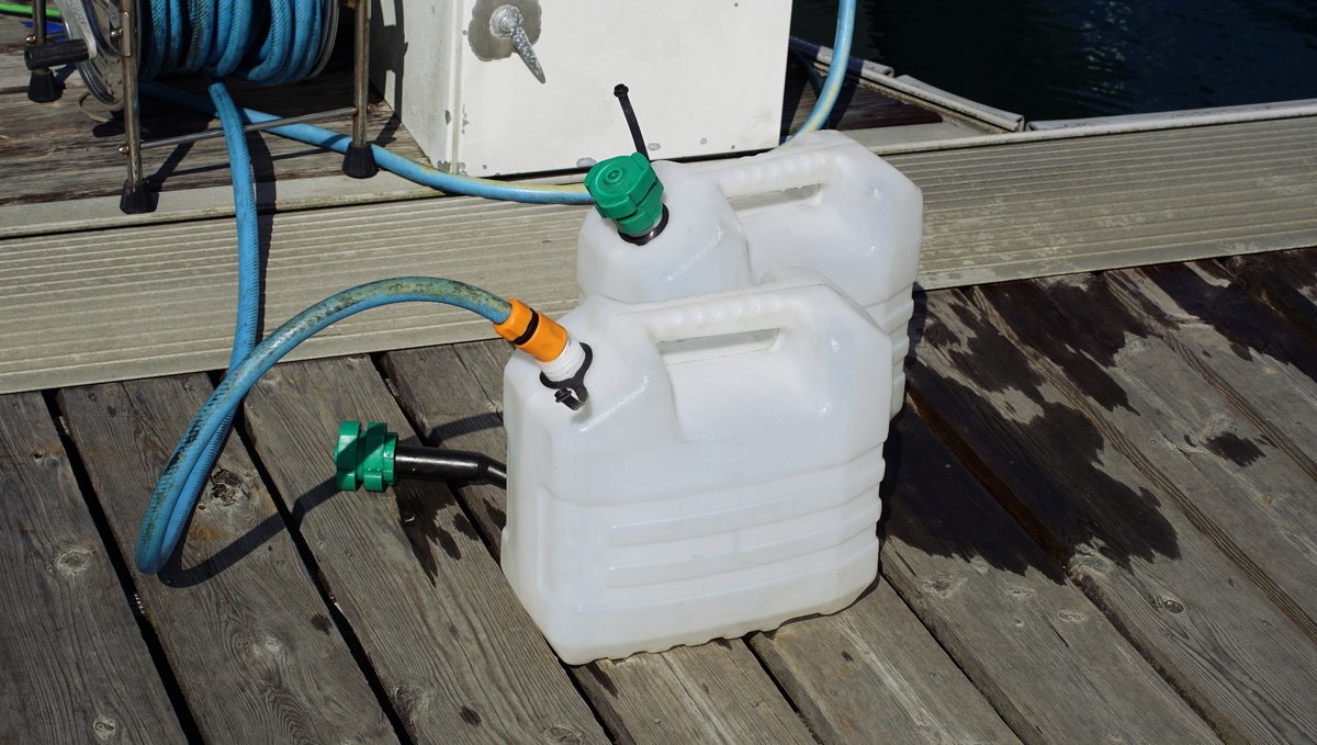Two jerry cans being filled with a hose on a dock.