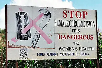 Billboard with surgical tools covered by a red X. Sign reads: STOP FEMALE CIRCUMCISION. IT IS DANGEROUS TO WOMEN'S HEALTH. FAMILY PLANNING ASSOCIATION OF UGANDA
