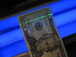 The security thread of a US $20 bill glows green under blacklight as a safeguard against counterfeiting.