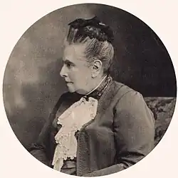 Black and white of a seated older woman in profile, her hair up, in a formal dark suit with a lace cloth at the neck