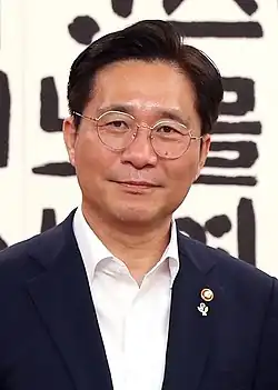 A picture of Sung Yun-mo in a black suit and white shirt, with two small badges pinned to the upper left lapel of his suit.