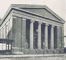 Black and white photograph of a building with columns, stairs leading to the street, and a neoclassical pediment