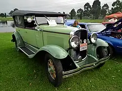 A lime-green 1920s style car with a black foldable top facing forward angled towards the photo's right on grass