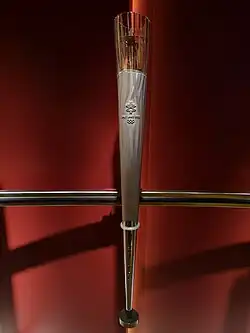 Tall and slender conical torch, composed of metal and glass, with the Olympic Rings logo, and the 2002 Winter Olympics logo