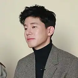 Kim facing right and wearing a black turtleneck and striped blazer.