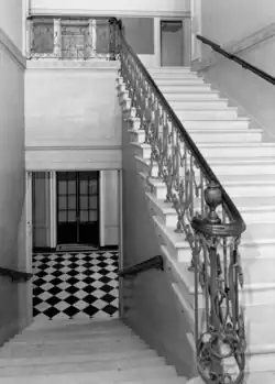 A grand stair in the Fahnestock house at 457 Madison Avenue. The image is taken from an intermediate landing; the flight of stairs to the left leads downward, while the flight of stairs to the right leads upward.