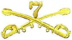 A computer generated reproduction of the insignia of the Union Army 7th Regiment of Cavalry. The insignia is displayed in gold and consists of two sheafed swords crossing over each other at a 45-degree angle pointing upwards with a Roman numeral 7