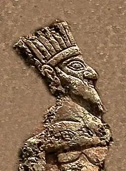 Depiction of a crown-wearing king, naked, imprisoned by Anubanini. This is possibly a feathered crown as seen on some bronzes of Luristan.[12][1]