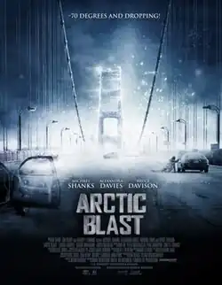 Poster for Arctic Blast. A dramatic, icy scene shows a suspension bridge engulfed in a fast-moving blizzard or freeze wave. Snow and ice dominate the environment, and abandoned vehicles line the bridge. In the distance, a freezing fog obscures the structure. The tagline at the top reads "-70 DEGREES AND DROPPING!" The title is centered in bold, icy letters. Cast members Michael Shanks, Alexandra Davies, and Bruce Davison are credited above the title.