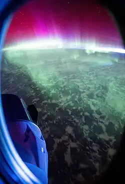 Crew Dragon Freedom illuminated in a blue glow as auroras move through Earth's atmosphere