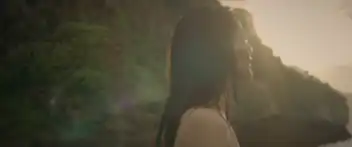 Maryam looking upwards to the skies whilst crying, in a naked state at a beach during sunset.