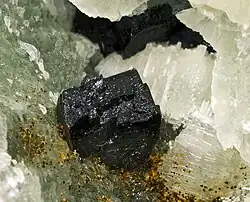 Shiny black crystals of babingtonite on whitish matrix.