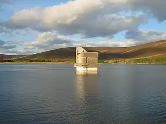 A lake with a pump house in the middle, surrounded by hills