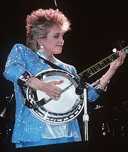 Barbara Mandrell, singing into a microphone while playing a banjo.