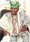 Oba Oladele Olashore is show in traditional Yoruba attire sitting on a chair