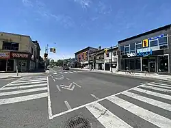 A large asphalt intersection with zebra markings for pedestrian crosswalks and a pedestrian bike lane.