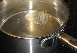 picture of a bell-shaped menstrual cup, covered in simmering water in a stainless cooking pot on a hob