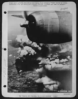 A black and white photograph of many grey clouds of smoke arising from the ground, the engine of the plane the photograph was shot from can also be seen