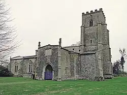 A stone church seen from the north east, with a battlemented tower, a large north porch, and the body of the church extending to the left