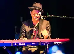 A smiling Mars onstage, seated at a keyboard
