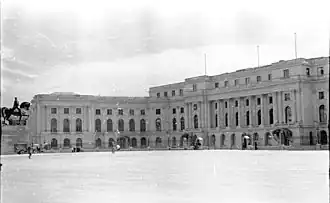 Large public building fronted by sentry boxes and a near-empty square.