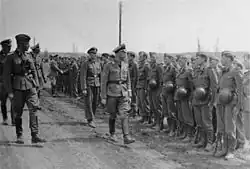 a black and white photograph of a bespectacled Heinrich Himmler in uniform walking along a line of soldiers in Waffen-SS uniform