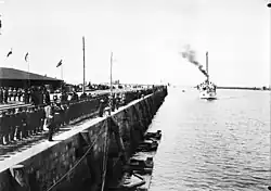A black and white photograph, from the front, of a ship approaching a harbor