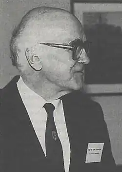 Black and white photograph, older man, balding, bespectacled, wearing a suit and a tie, looking to the side away from the viewer
