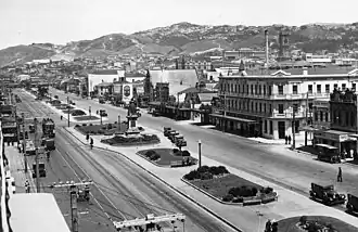 A black and white photograph of two urban streets with a strip of grass and walkways between them, with a statue of Queen Victoria on the divider.
