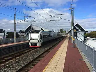 Electric multiple unit train at elevated train station with side platforms with small shelters on each platform
