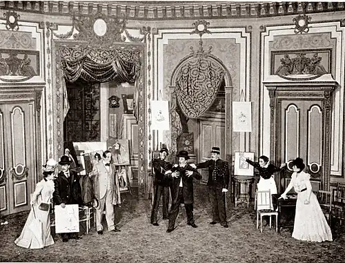 Stage scene with man in late 19th-century civilian clothes being arrested by two gendarmes
