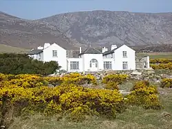 Charles Boycott's house on Achill Island. It is a large white house with two storeys. The mountainous terrain on the island is seen in the background.
