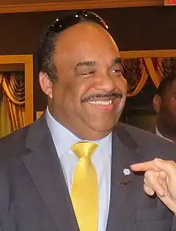 Head shot of Young smiling, wearing a dark suit jacket with a Democratic Party lapel pin and yellow necktie.