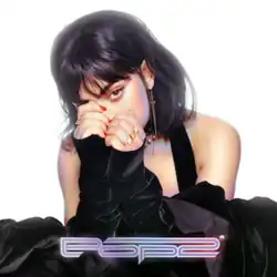 Charli XCX is wearing a black dress, hiding half of her face with her curled up hands against a white background. The words "Pop 2" are placed at the bottom of the singer.