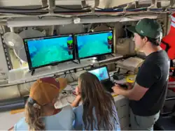 Two children and an adult man viewing television monitors
