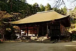 Wooden building with a hipped roof, slightly raised floor, an enclosing veranda and a wide central staircase on the front.