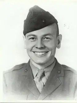 A young man dressed in his military uniform and wearing a Marine Corps style hat. He is smiling.