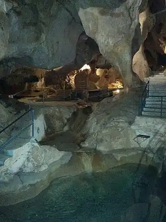 Rocky cave walls over a small lake surrounded by modern railings. There is a staircase to the right.