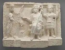 Limestone relief sculpture with three figures, the one on the right (in military dress) holding a crown over the head of the figure in the middle.