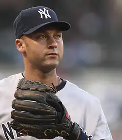 Derek Jeter wearing a navy hat and gray baseball uniform with a black glove stares into the distance.
