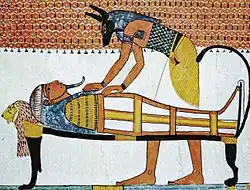 Painting of a jackal-headed god bending over a mummy on a bier