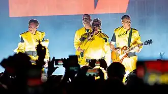 Devo onstage, wearing their trademark bright yellow radiation suits