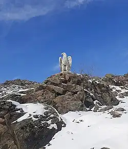 A picture of an eagle sculpture set on a rock, taken against a clear blue sky