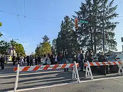 Fraser Street south of East 41st Avenue. Traffic is blocked off with barricades, and a crowd of police officers and members of the public can be seen in the background.