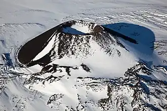 A partially snow-covered, cone-shaped volcano with a bowl-shaped crater on its top.