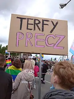 Person in a crowd holding a placard showing "TERFY PRECZ" (TERFS OUT in Polish)