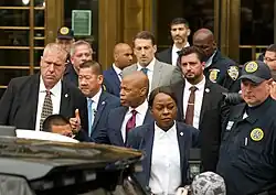 Eric Adams giving a thumbs up to reporters out of frame, and surrounded by officials.