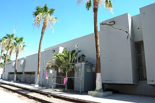 A white building in Calexico with a crack on one of its walls. There are palm trees in front of the building.