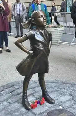 A bronze sculpture of a girl looking forward and up, with her hands on her hips